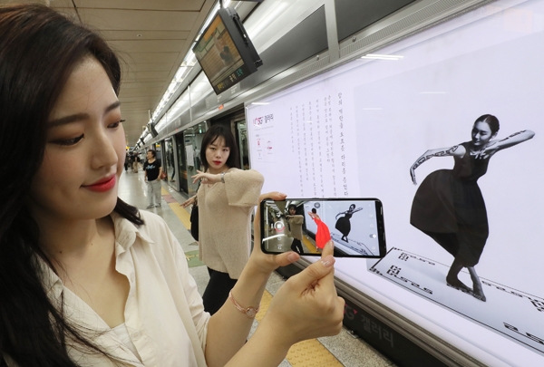 한 여성이 스마트폰으로 공덕역에 설치된 ‘리슨 투 더 댄스’를 감상하고 있다(왼쪽). 여성이 오른손 검지로 가리키는 동영상은 구글 렌즈 앱을 이용한 증강현실 기술을 통해서만 볼 수 있는 작품이다.