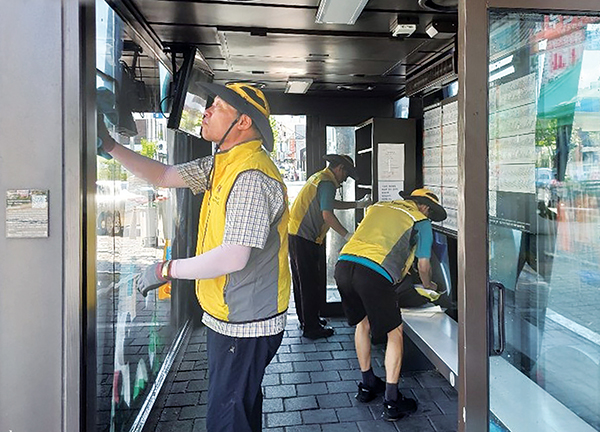 오네시모봉사단원들이 버스정류장 대기공간에 설치된 작은도서관 책장을 청소·소독하고 있다.